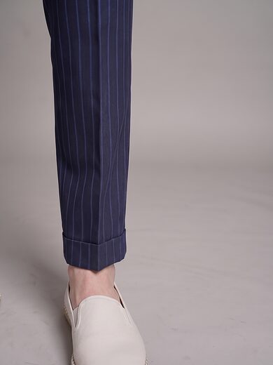 Close detail of the navy pinstripe trouser's turn-up cuff breaking over a cream slip-on shoe